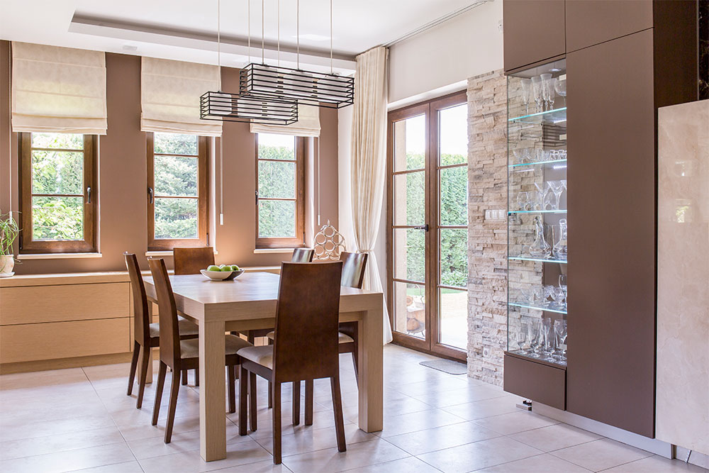 Elegant dining room featuring wooden dining table and chairs, modern roller shades on windows, stylish pendant lighting, and a glass display cabinet, emphasizing contemporary home decor.