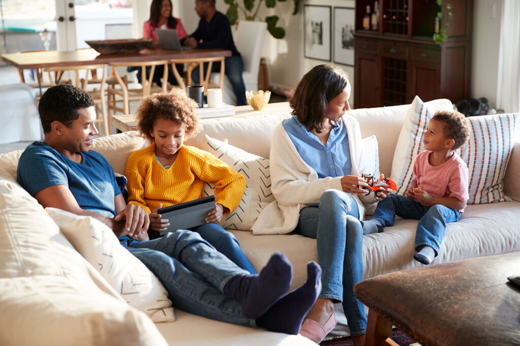 Family enjoying quality time together in a cozy living room, engaging with a tablet and toys, highlighting home comfort and togetherness, relevant to plantation shutter installation and home improvement themes.