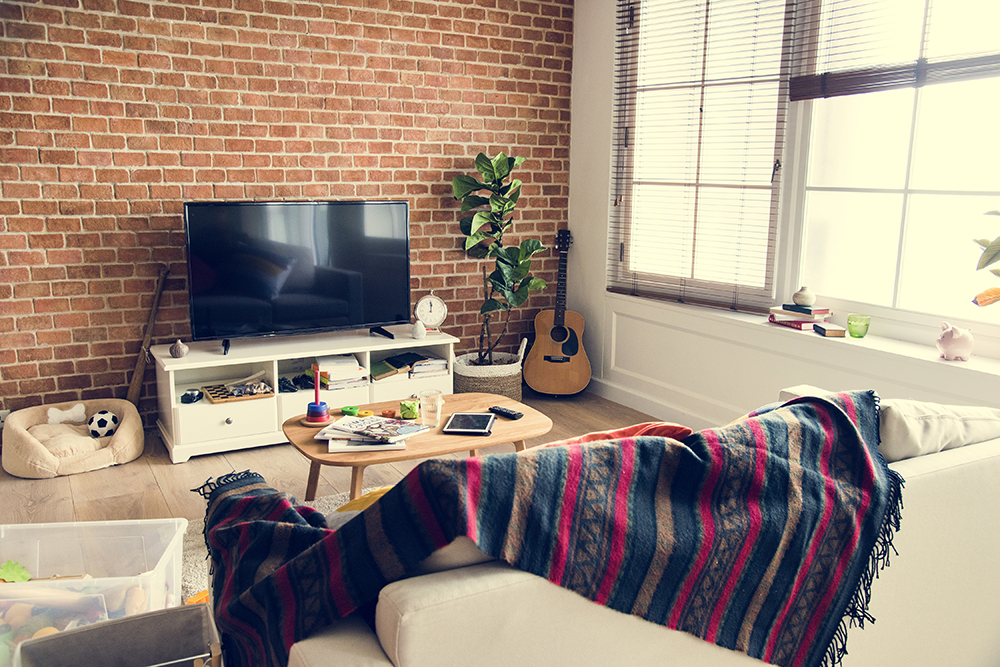 Cozy living room featuring a television, wooden coffee table, and a guitar, with a colorful blanket draped over a sofa, showcasing a warm and inviting atmosphere ideal for indoor relaxation and lighting control.