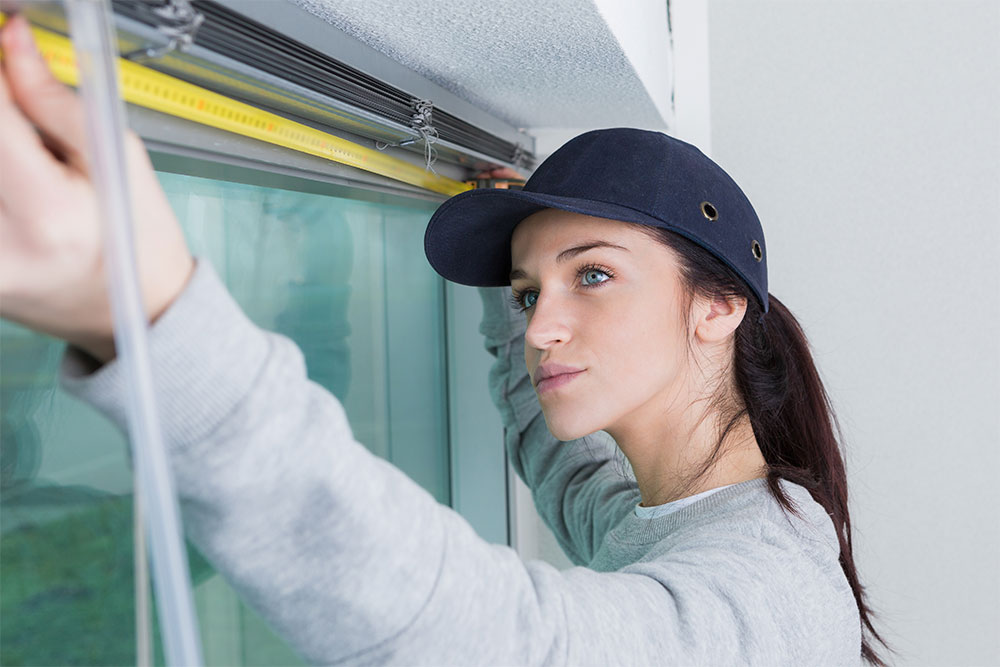 Woman measuring a window for plantation shutters installation, using a measuring tape and focused on precise measurements.