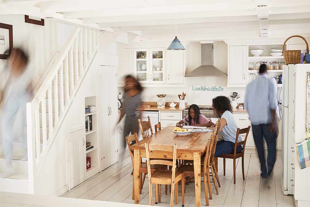 Family gathering in a bright kitchen, examining a checklist at a wooden dining table, with individuals moving around, emphasizing home preparation for cold weather.