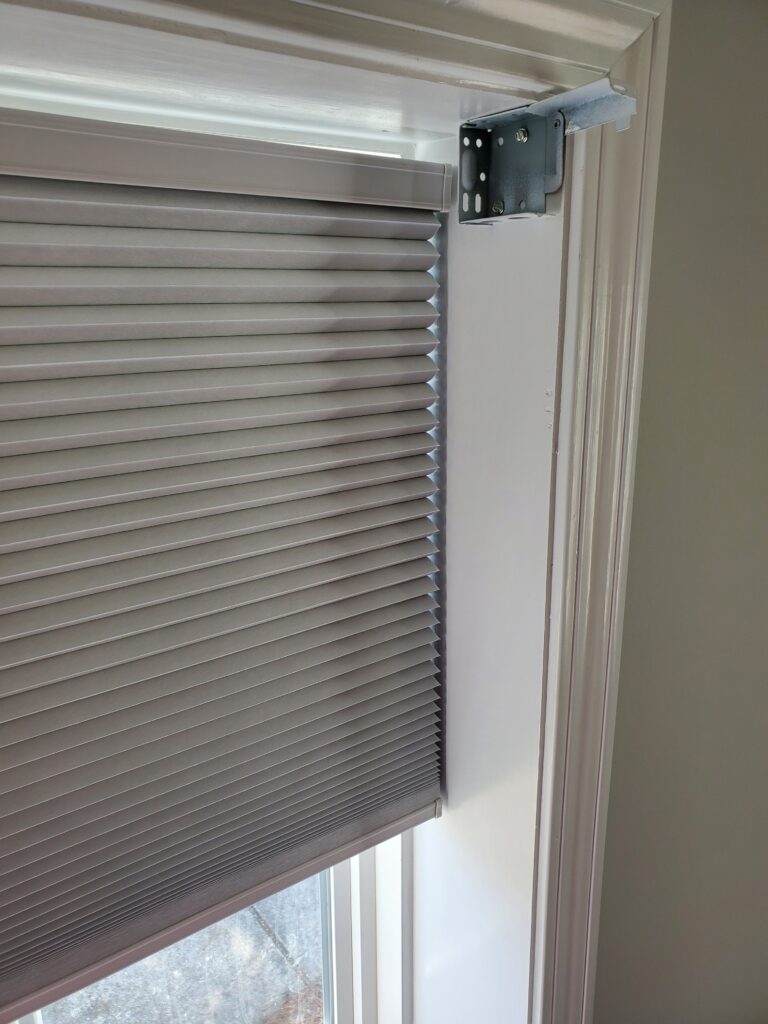 Close-up of a window with modern gray blinds installed, showcasing the hardware and clean lines, relevant to plantation shutters and window treatments offered by Plantation Shutter Pros.