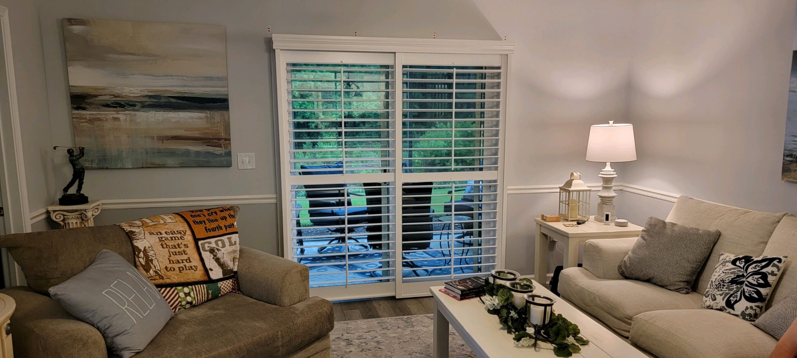Living room featuring energy-efficient plantation shutters, cozy seating, decorative pillows, and a view of the outdoor patio, emphasizing comfort and style.