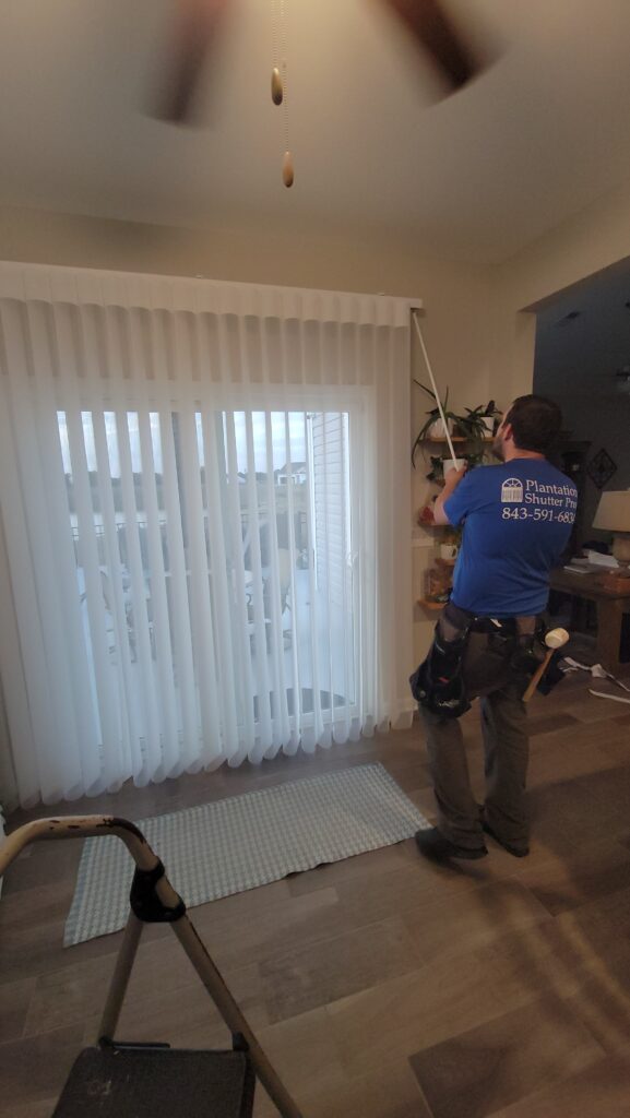 Technician installing vertical blinds in residential space, showcasing plantation shutters and window treatments from Plantation Shutter Pros.