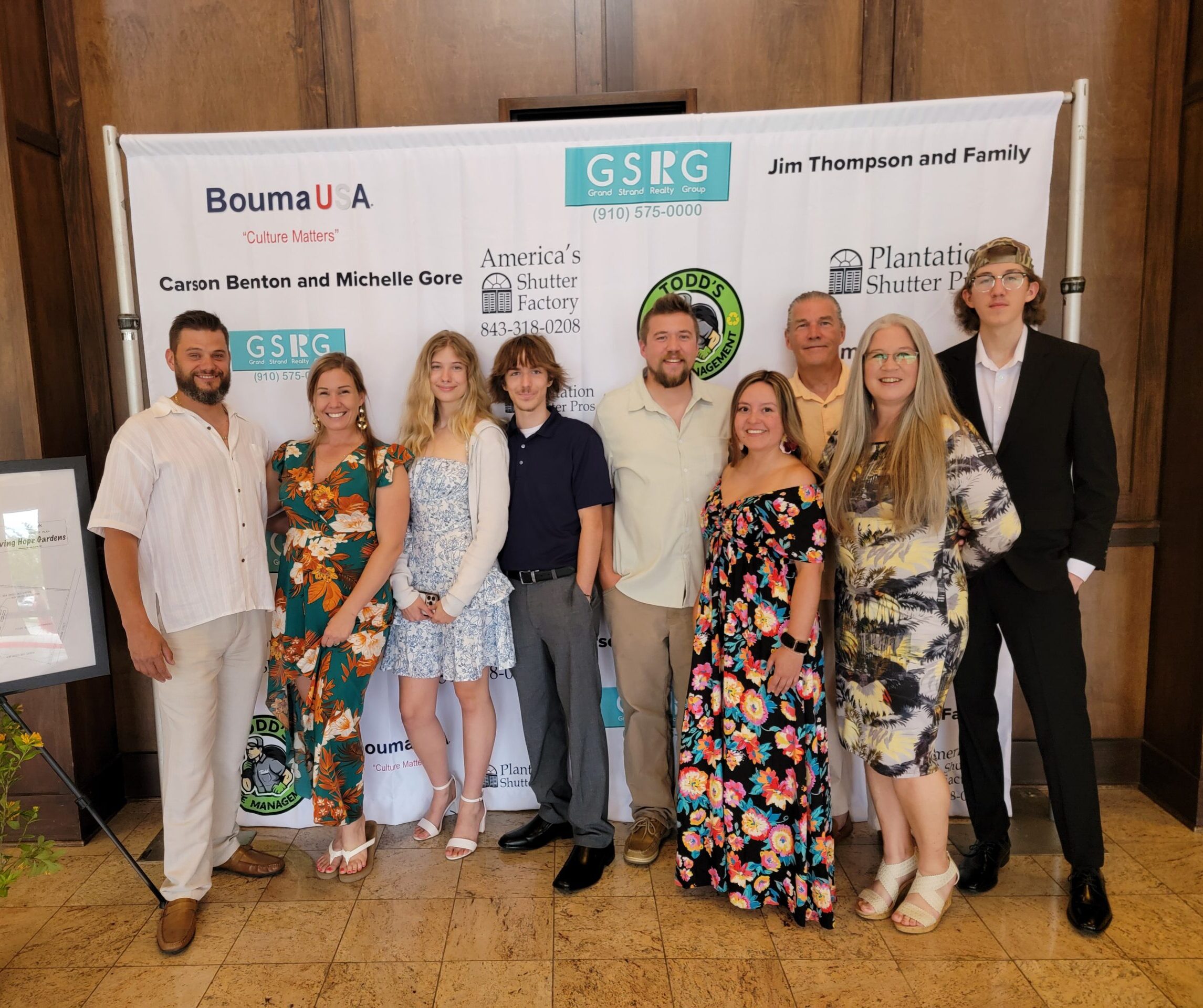 Group of individuals posing in front of a promotional backdrop featuring Plantation Shutter Pros, celebrating community connections and local partnerships in Myrtle Beach.