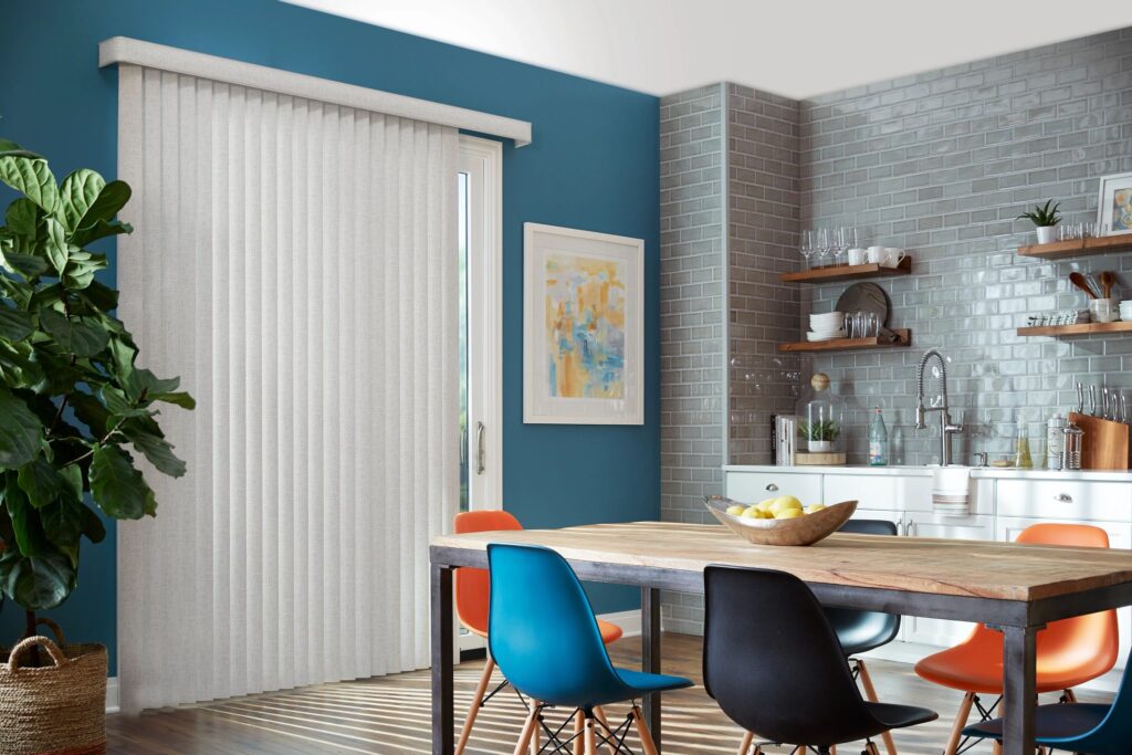Vertical blinds in a modern kitchen setting with a blue accent wall, featuring a wooden dining table and colorful chairs, showcasing an inviting home ambiance.
