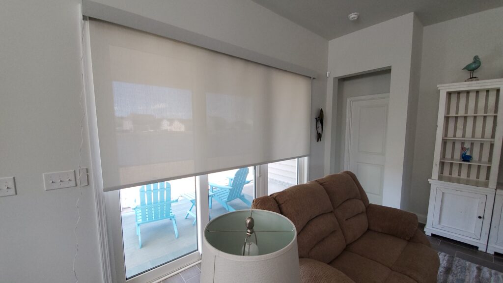 Living room featuring light-filtering window shades, beige couch, and aqua blue outdoor chairs visible through the window, showcasing a modern and inviting interior design.