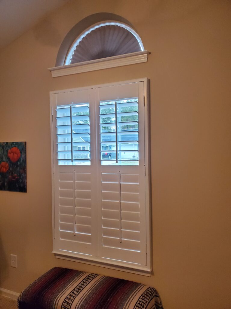White plantation shutters with arched top, enhancing natural light in a cozy interior space, showcasing window treatment options for home aesthetics.