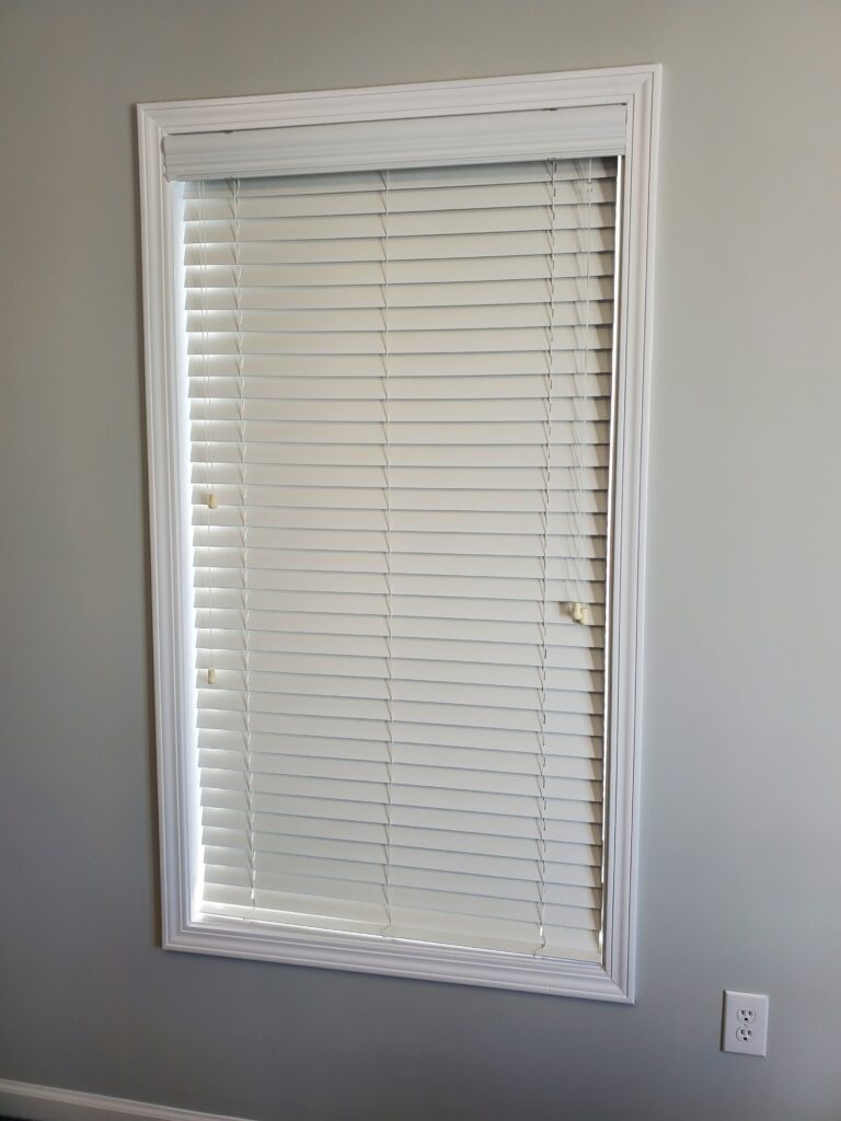 White faux wood blinds installed in a window frame, enhancing interior aesthetics and light control, relevant to window treatment options from Plantation Shutter Pros.