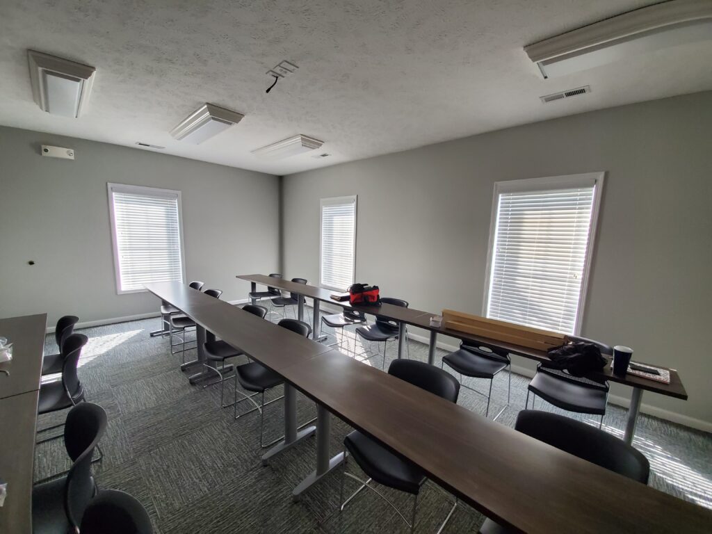Interior view of a meeting room featuring multiple tables and chairs, with natural light streaming through window treatments, showcasing plantation shutters.