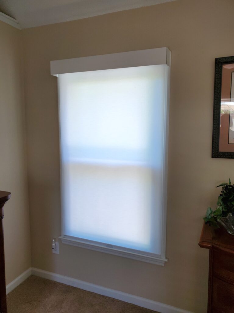 Window with sheer roller shade in a cozy room, showcasing modern window treatment options from Plantation Shutter Pros.