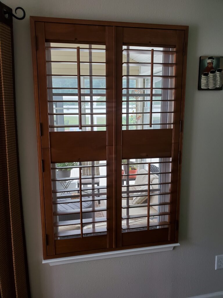 Wood plantation shutters with horizontal slats, partially open, revealing a bright outdoor space and indoor seating area, showcasing a stylish window treatment option for enhancing home aesthetics.