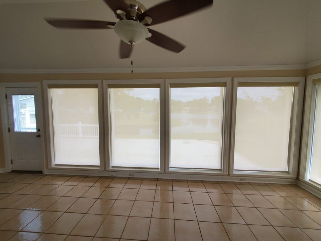 Interior view of a sunroom featuring large windows with sheer window shades, tiled floor, ceiling fan, and a door leading outside, showcasing a bright and airy atmosphere ideal for window treatment inspiration.
