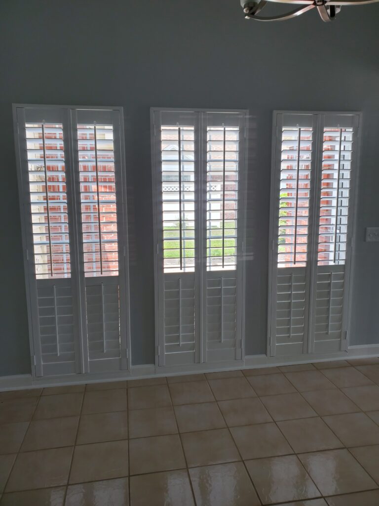 Three white plantation shutters installed on a light gray wall, showcasing a modern window treatment design for enhancing residential spaces.
