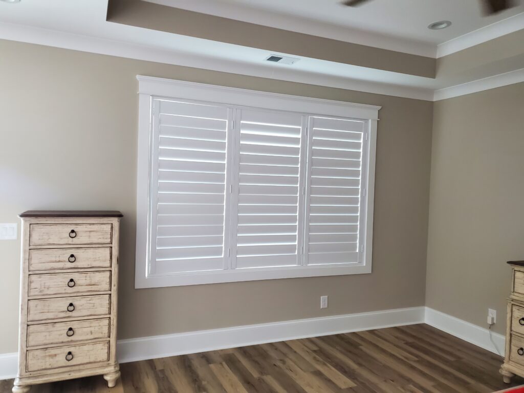 White plantation shutters installed on a window in a modern room with light-colored walls and wooden flooring, showcasing a stylish window treatment option.