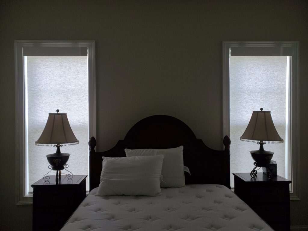 Bedroom featuring two window shades, bedside lamps, and a wooden bed frame with pillows, showcasing window treatment options for home decor.