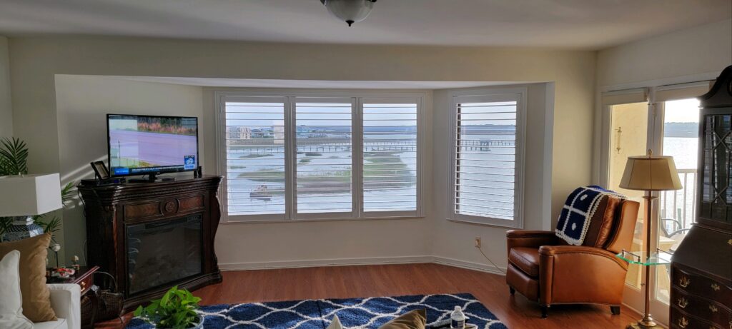 Living room featuring hybrid plantation shutters, a cozy leather armchair, and a view of the water, showcasing stylish window treatments and home decor.