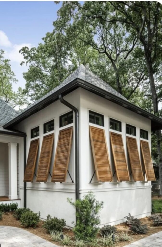 Exterior view of a house featuring wooden plantation shutters on windows, surrounded by greenery and landscaping, emphasizing window treatment options for enhancing home aesthetics.