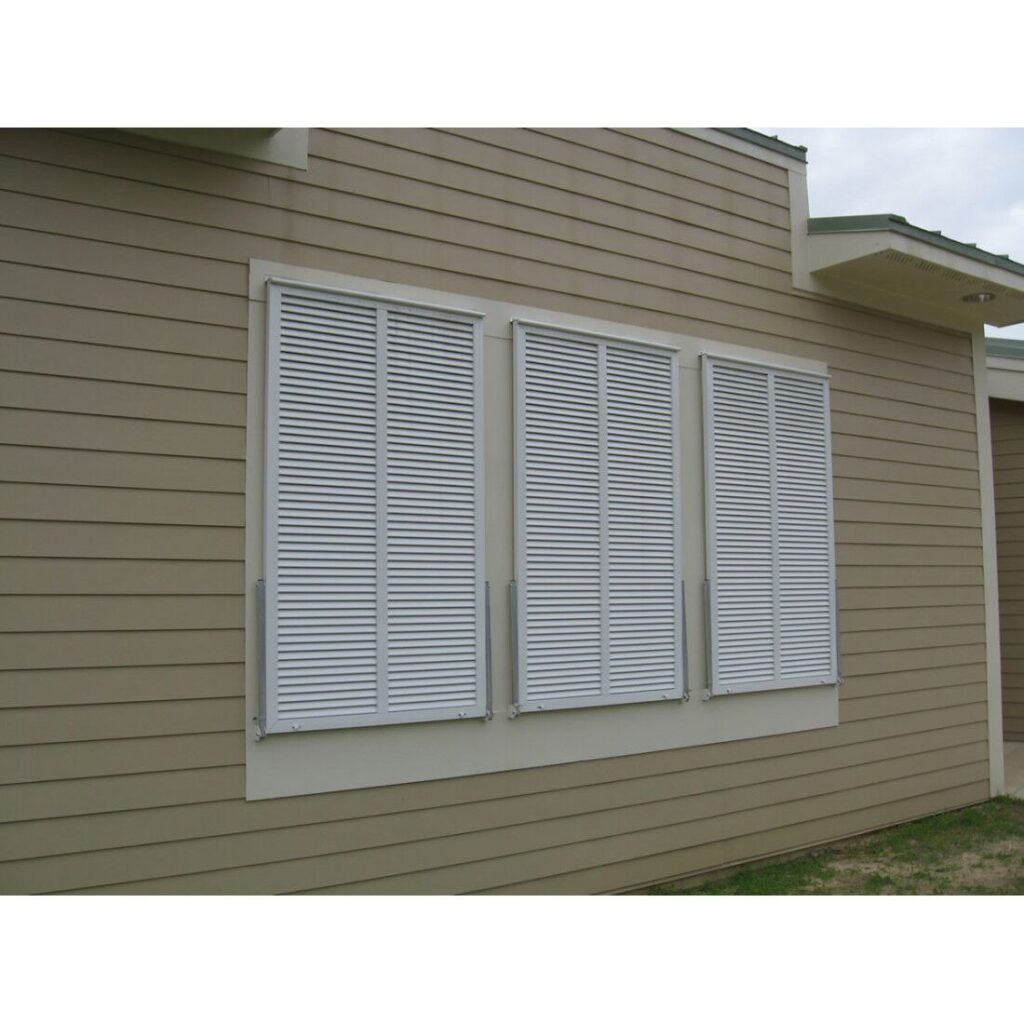 Bahama impact hurricane shutters with articulated blades installed on a beige house exterior, showcasing window protection and aesthetic appeal.