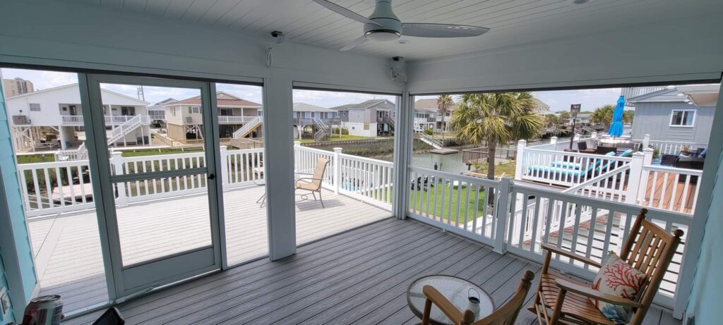Spacious sunlit porch with sliding glass doors, showcasing a scenic view of a waterfront area, featuring palm trees, residential homes, and a pool, ideal for enhancing interior outdoor living spaces.