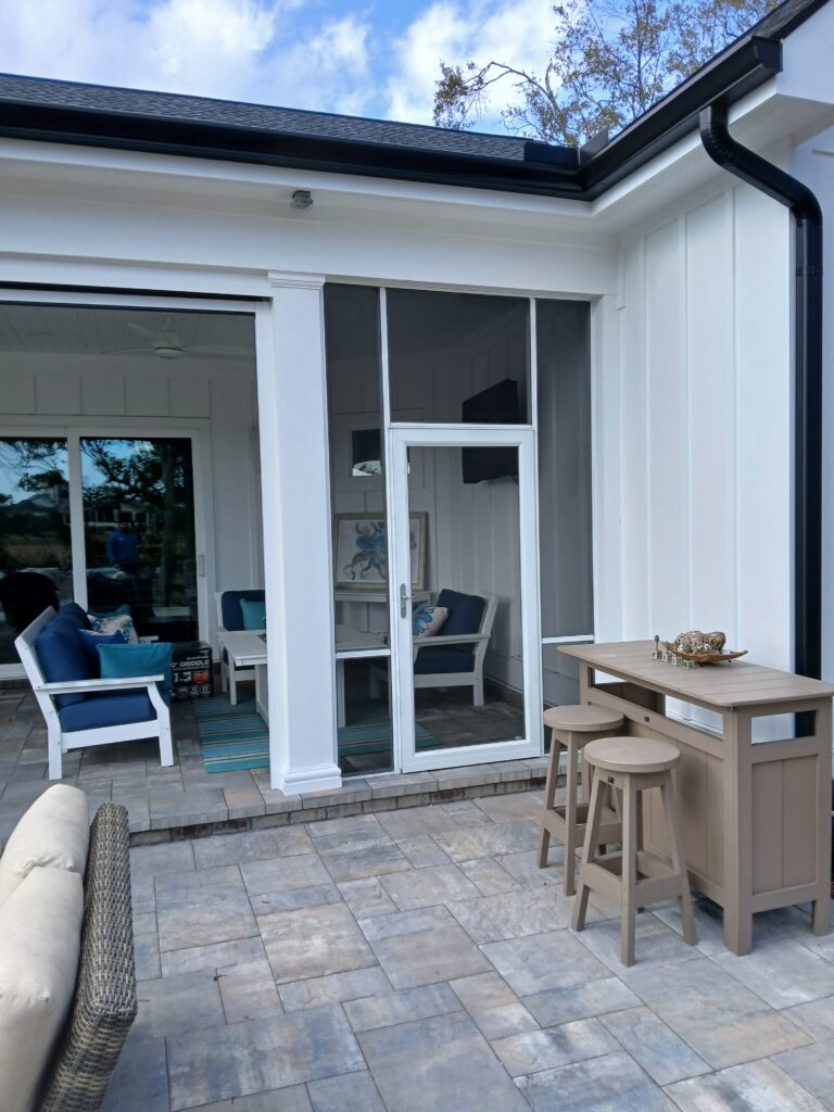Outdoor living space featuring a screened porch with blue seating, a light-colored bar table, and stools on stone flooring, showcasing window treatment options for enhancing home aesthetics.