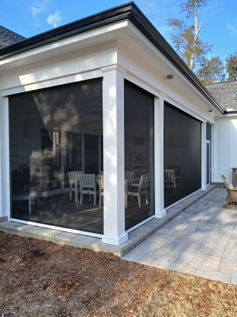 Exterior view of a modern home featuring large black solar screens, showcasing a stylish outdoor seating area with white furniture, enhancing outdoor living space aesthetics.