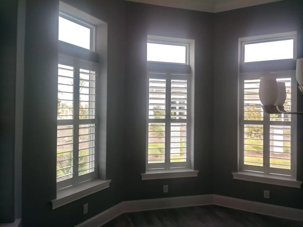 Three large windows with white shutters in a modern room.